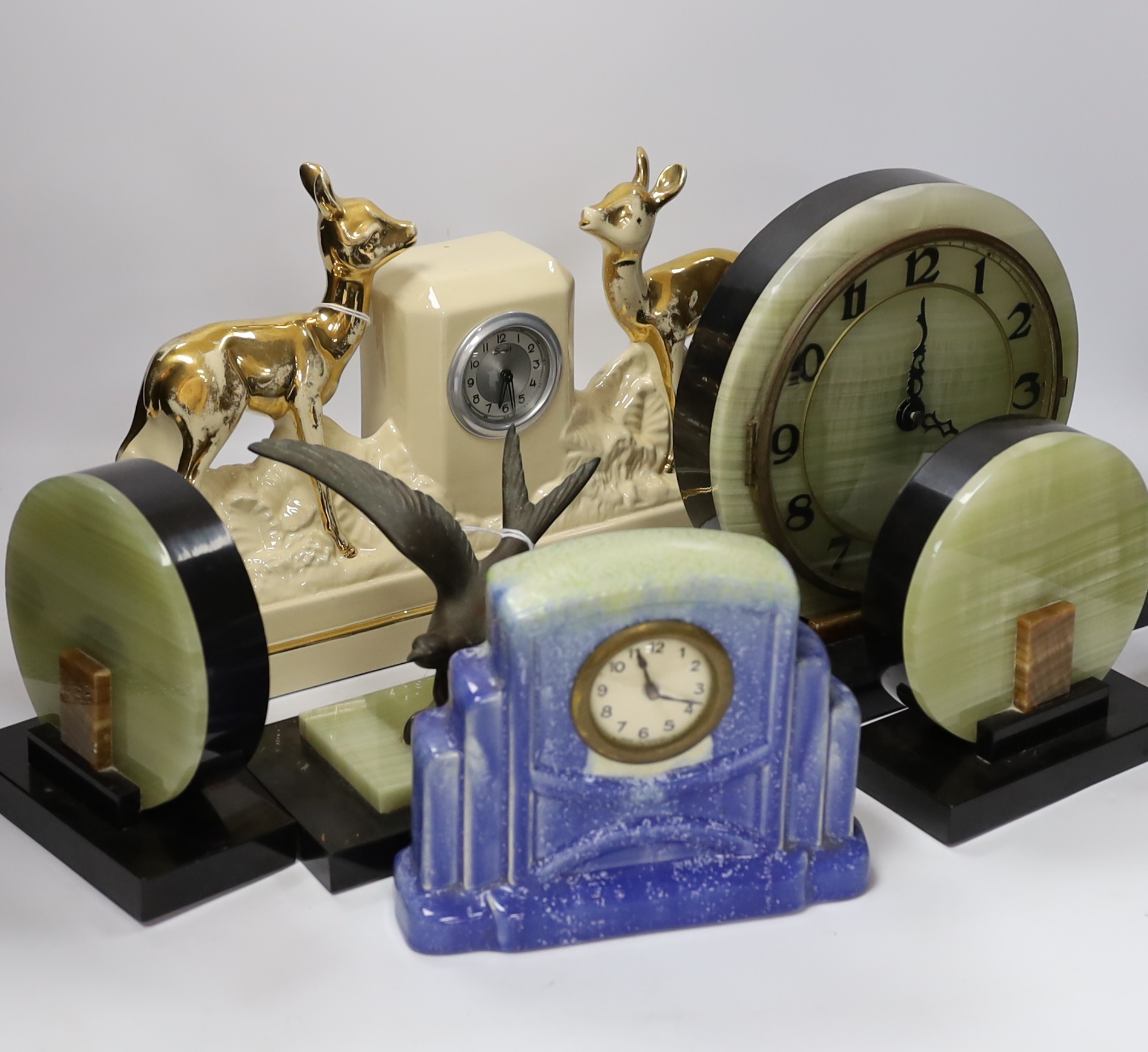 A French Art Deco green onyx clock garniture with bluebird spelter mount, together with two French ceramic mantel timepieces, largest 46cm wide